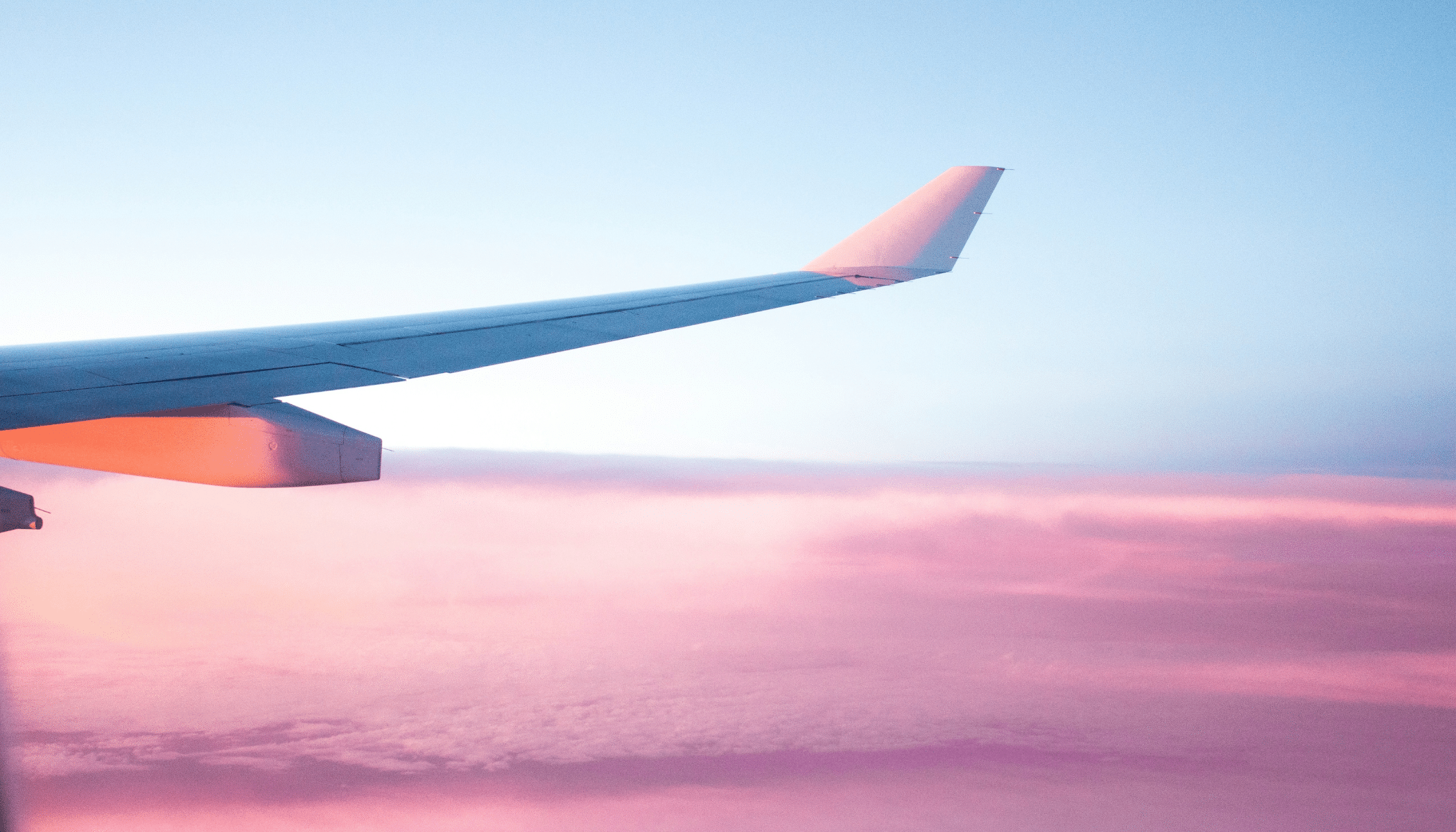 Wing of an aeroplane with sunset light across it, with pink clouds and a blue sky in the background